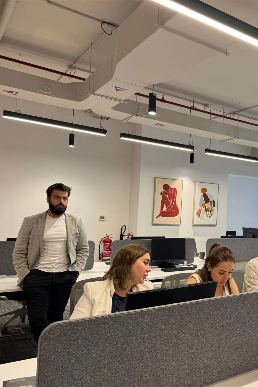 Équipe au travail dans un open space moderne : un homme en veste debout près de collègues concentrés devant leurs écrans