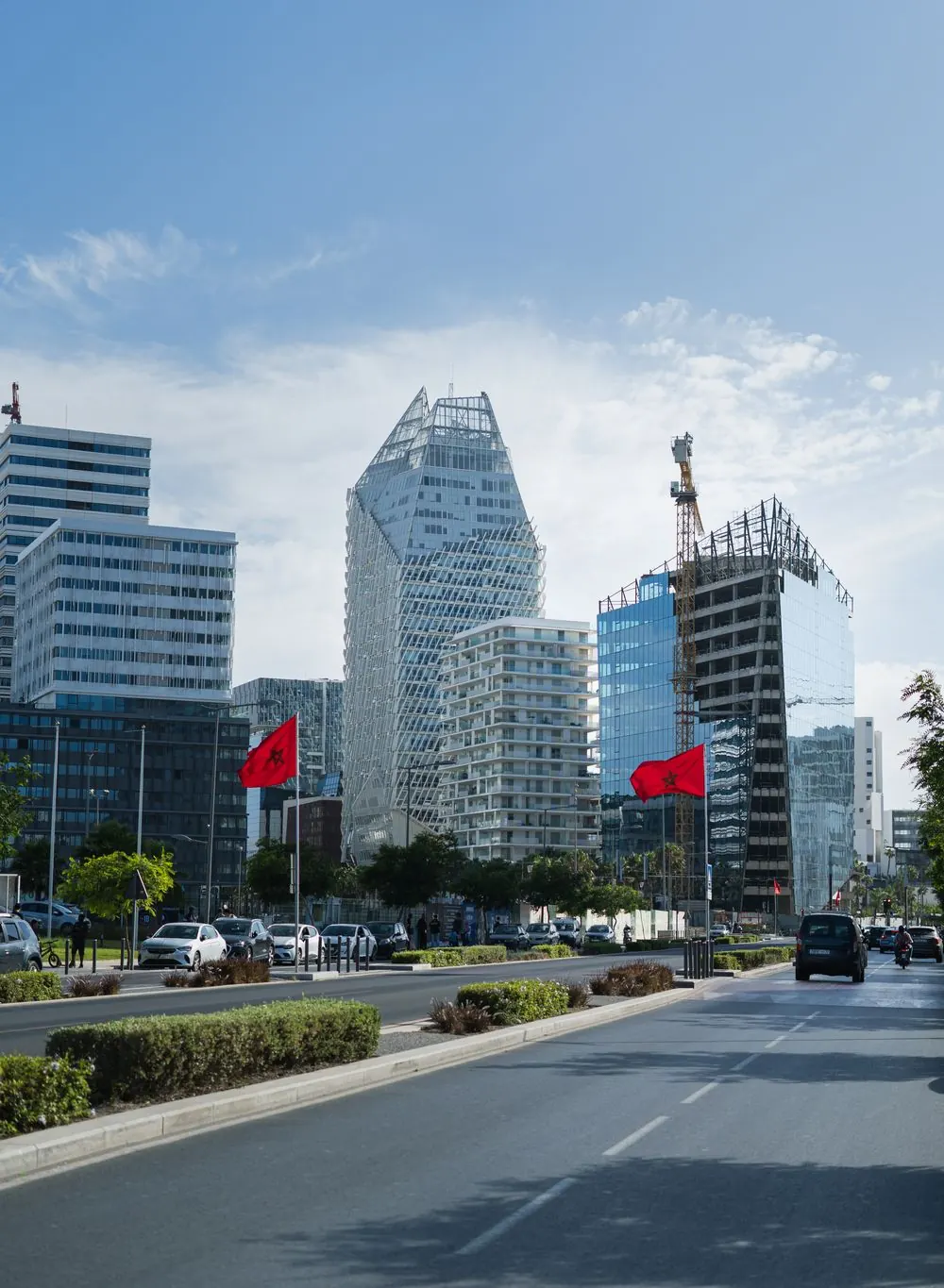 Avenue et tours modernes d'un quartier d'affaires marocain, drapeaux rouges flottant sous un ciel bleu